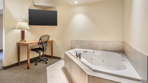 A modern bathroom with a large bathtub, a desk with a chair, and a mounted flat-screen TV. - Best Western Plus Service Inn & Suites (Lethbridge)