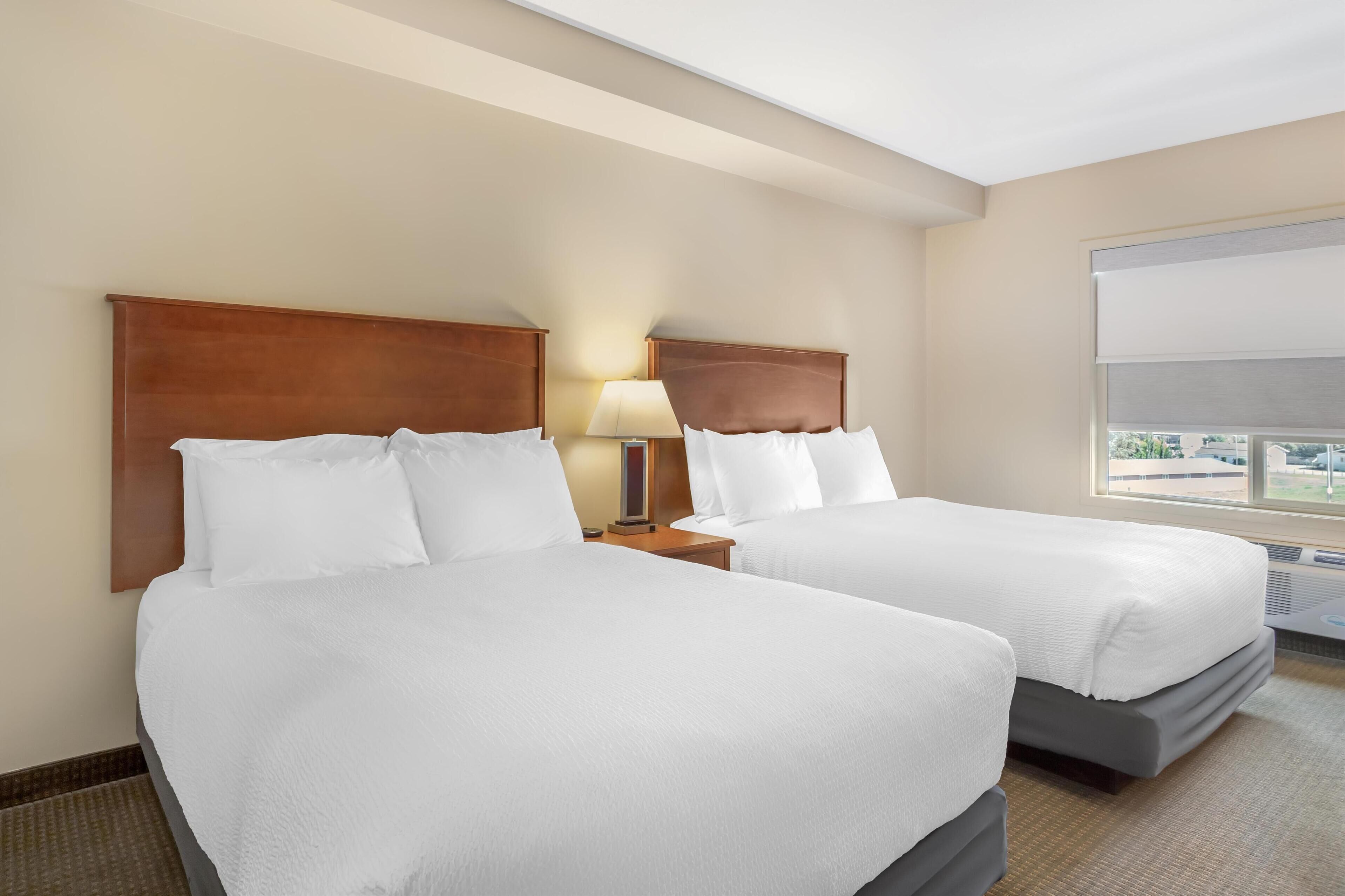 Een hotelkamer met twee bedden, een nachtkastje met een lamp en een groot raam met uitzicht op buiten.