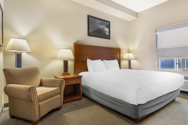 A hotel room with a large bed, two bedside lamps, a wooden nightstand, a chair, and a framed picture on the wall. - Best Western Plus Service Inn & Suites (Lethbridge)