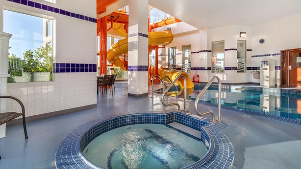 An indoor swimming pool with a hot tub, a slide, and a seating area with a view of the outdoors. - Best Western Plus Service Inn & Suites (Lethbridge)