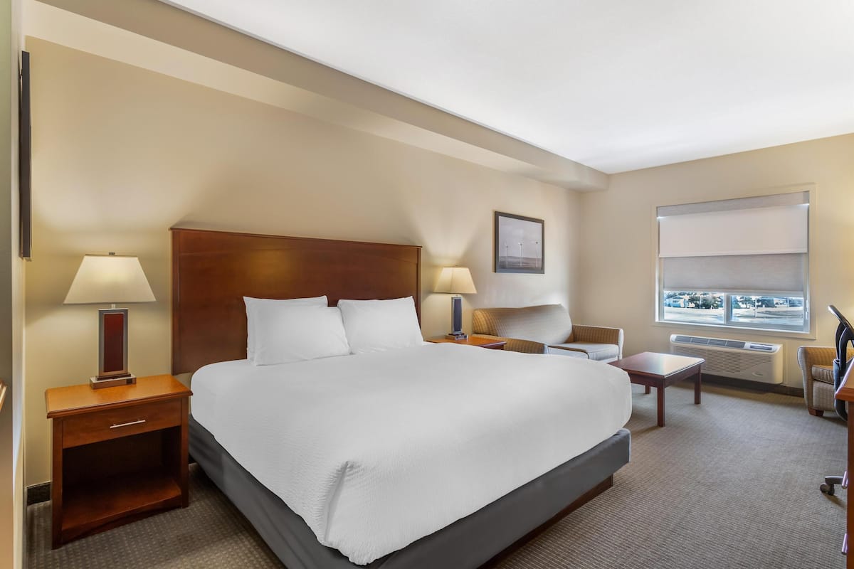 A hotel room with a large bed, two bedside tables with lamps, a small table, and a window with a view.