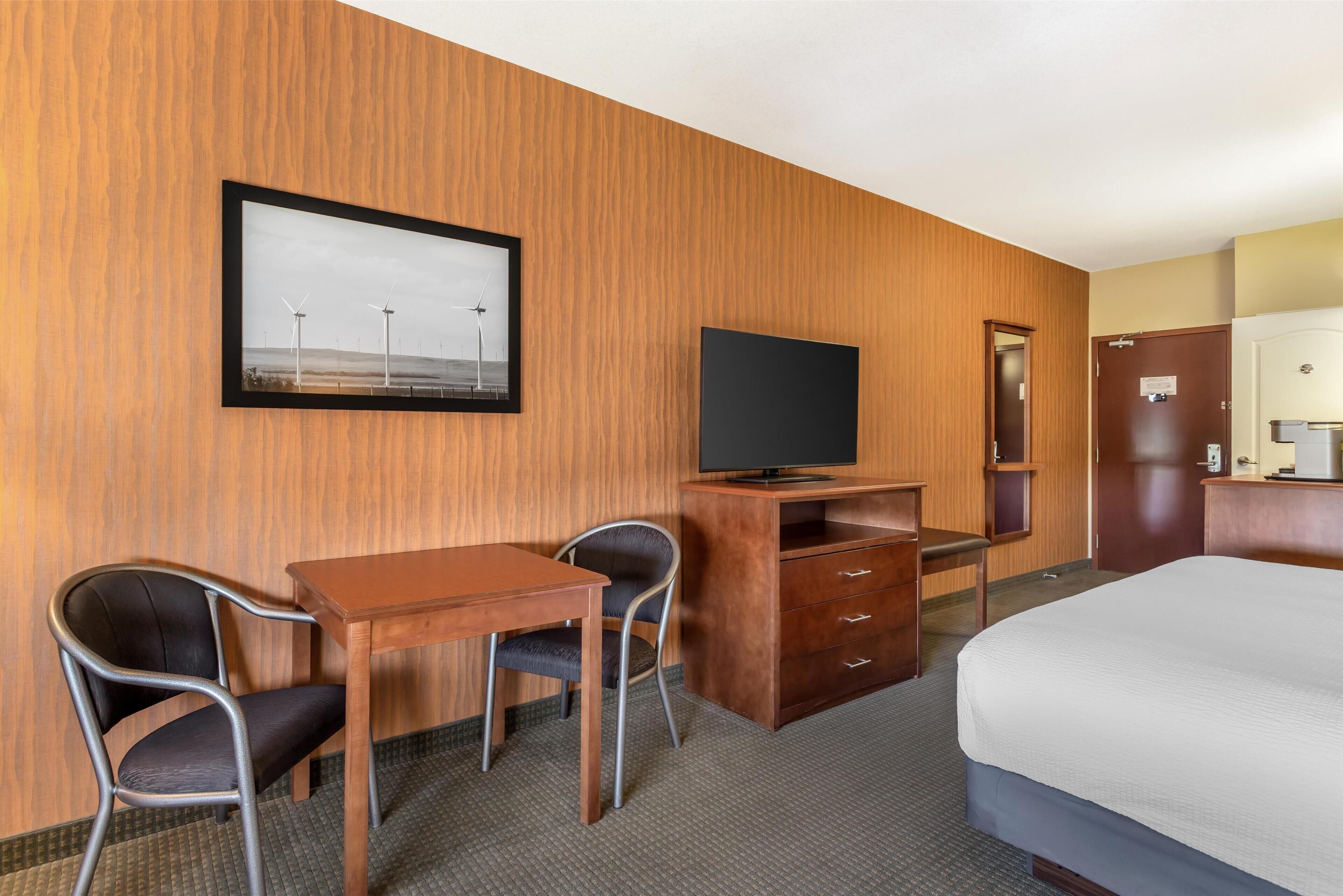 A hotel room with a wooden wall, a bed, a desk with a chair, a television, and a mirror.