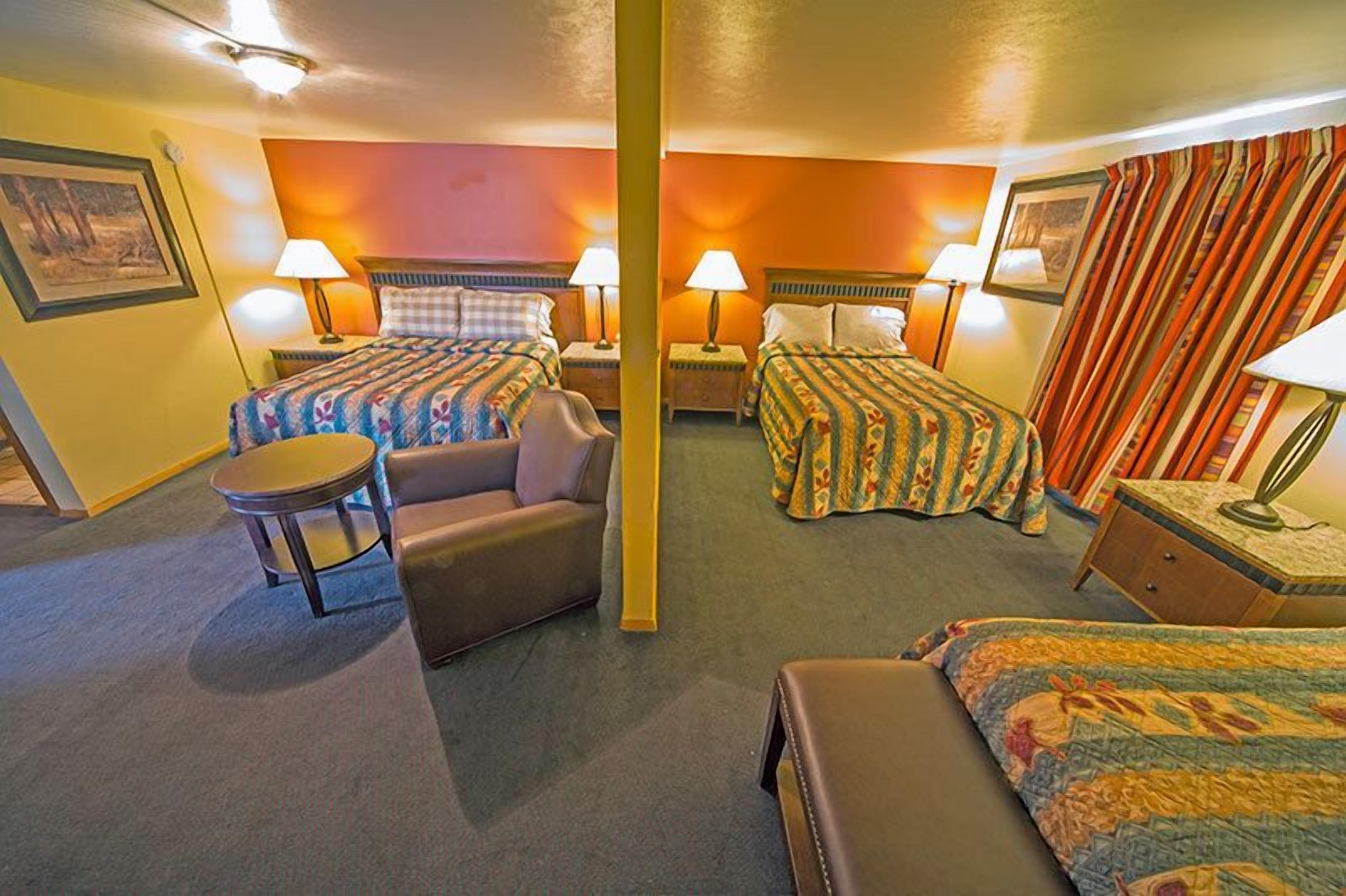 A hotel room with two beds, a sofa, a small table, and lamps.