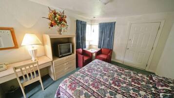 Una habitación de hotel con cama, escritorio con lámpara, televisión, silla y puerta.