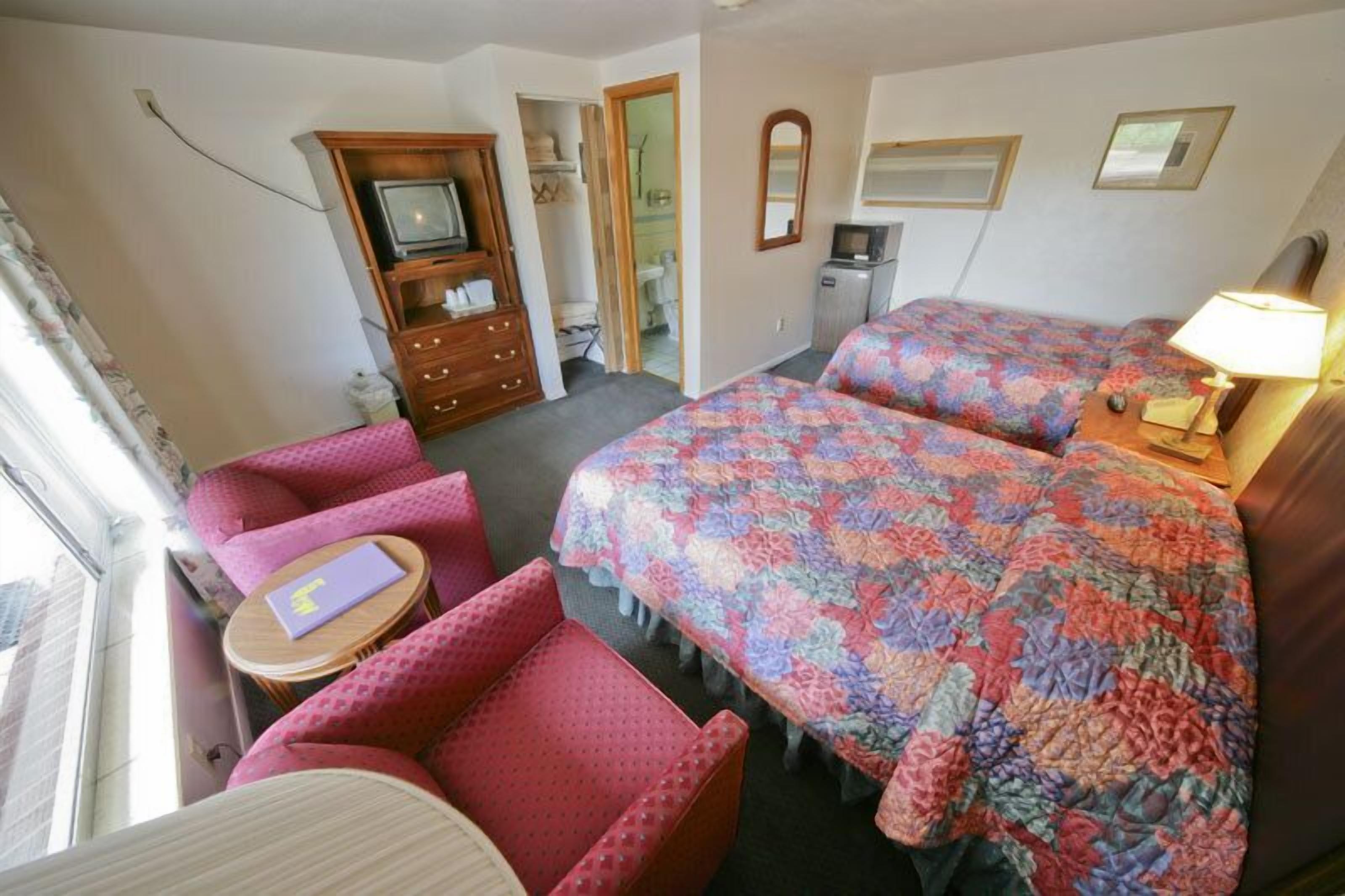 A hotel room with two beds, a desk, a chair, a TV, and a bathroom visible through an open door.