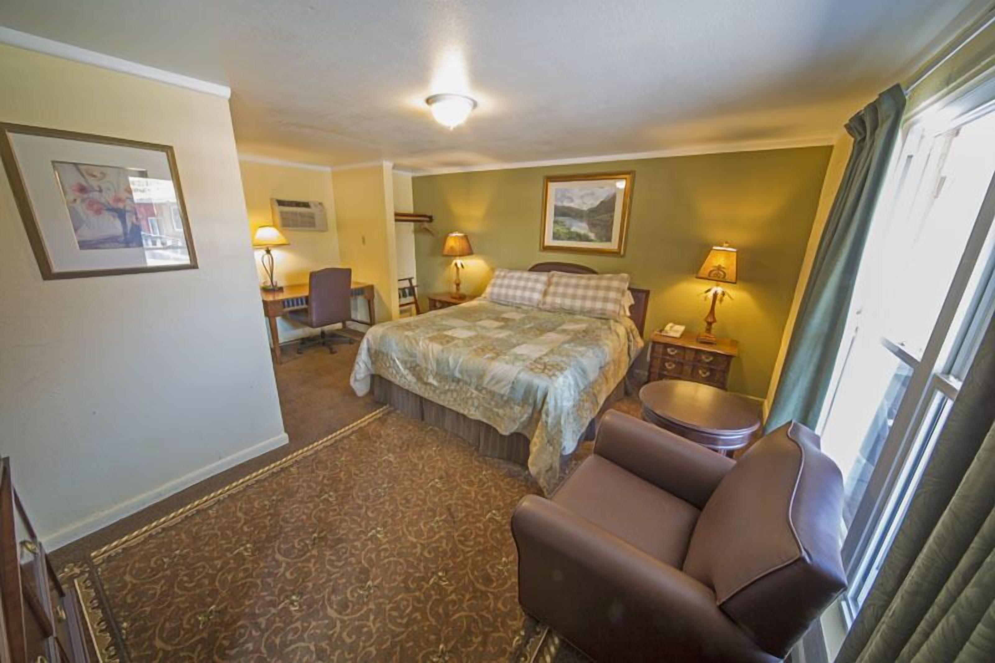 A hotel room with a bed, two bedside tables with lamps, a desk with a chair, and a window with curtains.