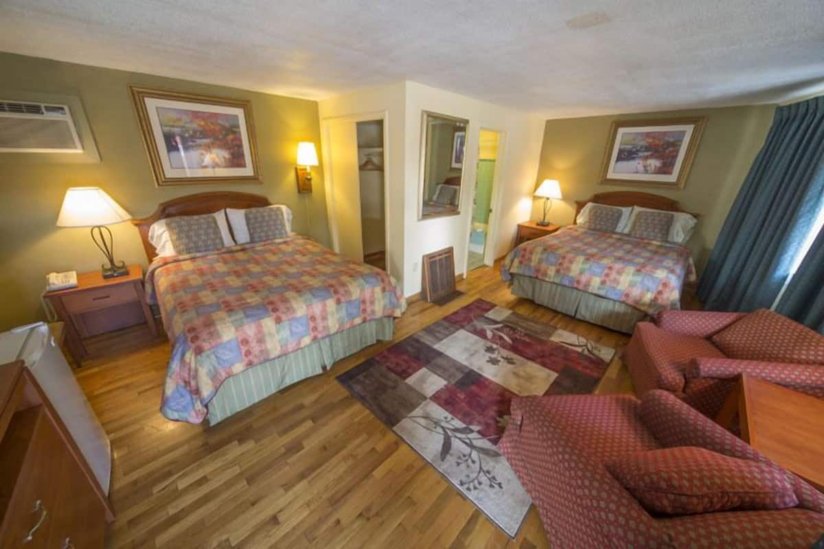 Ein Hotelzimmer mit zwei Betten, Holzboden, einem roten Sofa und einem großen Fenster mit Vorhängen.