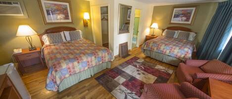 A hotel room with two beds, a wooden floor, a red sofa, and a large window with curtains.