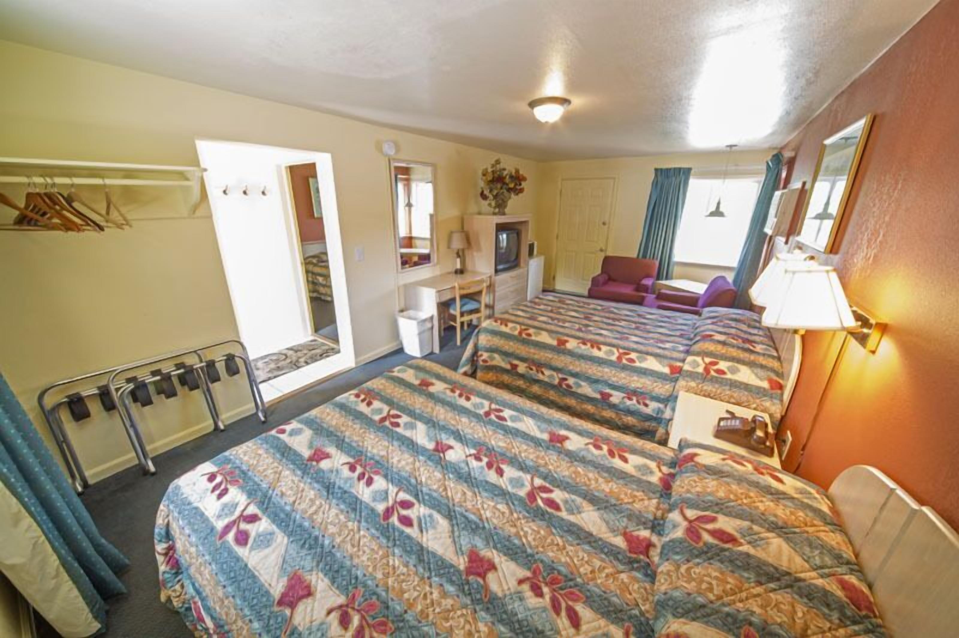 Une chambre d’hôtel avec deux lits, un bureau avec une chaise, une télévision et un miroir.