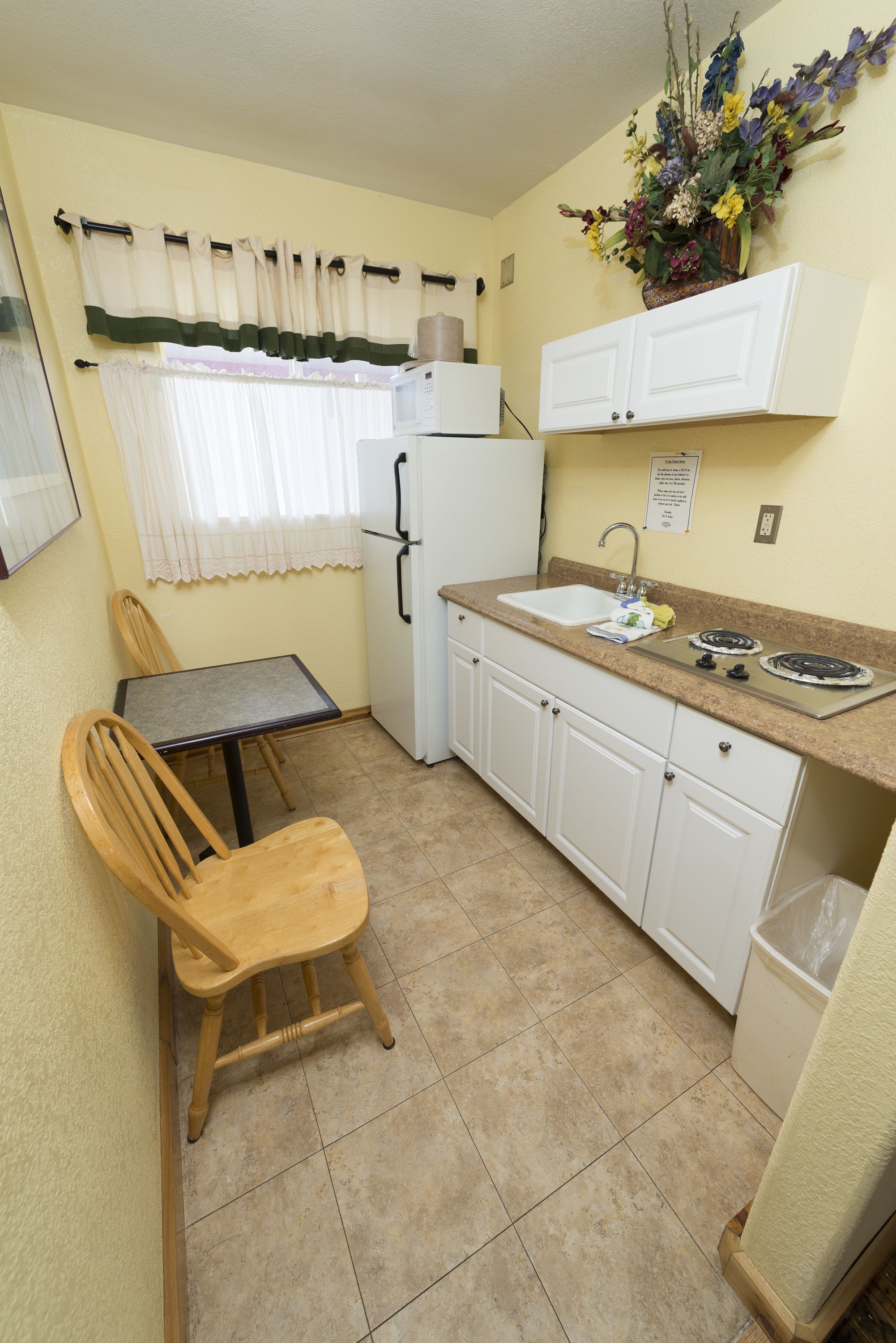 A compact kitchen with a dining table, chairs, a refrigerator, a sink, and cabinets.