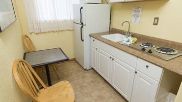 A compact kitchen with a dining table, chairs, a refrigerator, a sink, and cabinets.