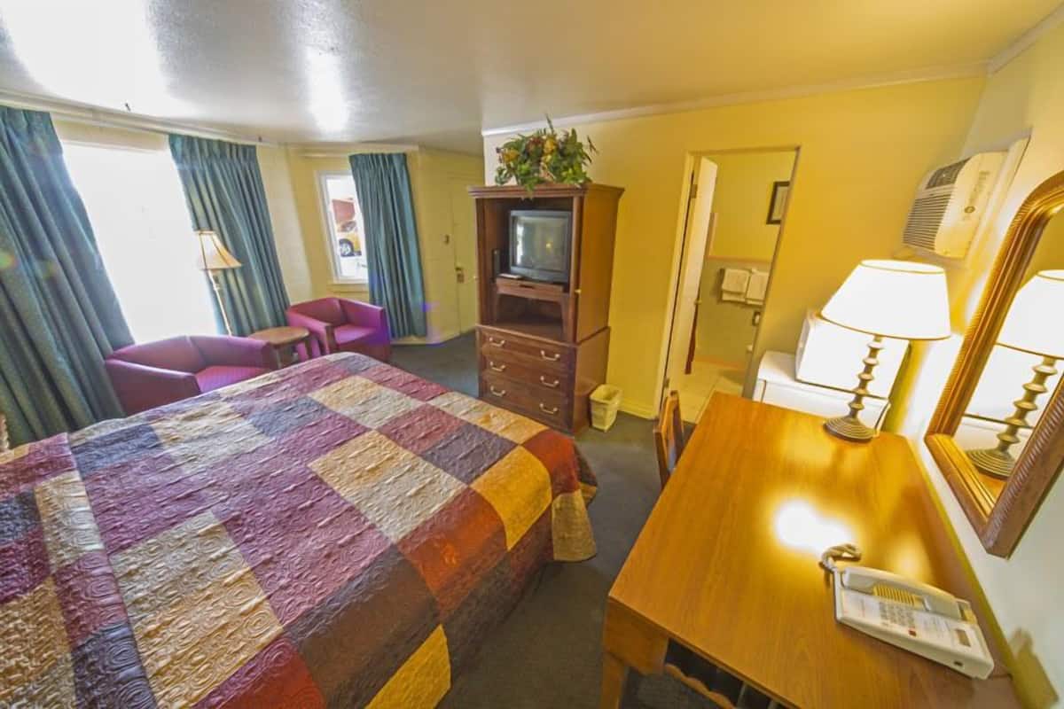 Ein Hotelzimmer mit einem großen Bett, einem Holztisch, einem Fernseher, einem Telefon und einem Spiegel.