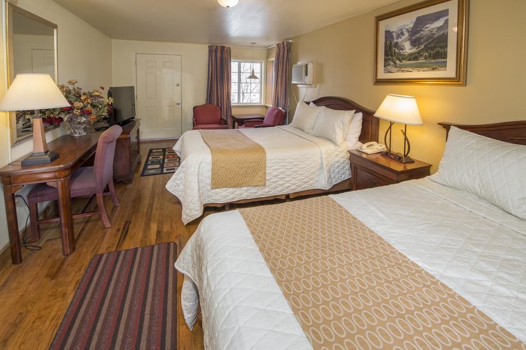 A hotel room with two beds, a desk with a lamp, a chair, a TV, and a painting on the wall.