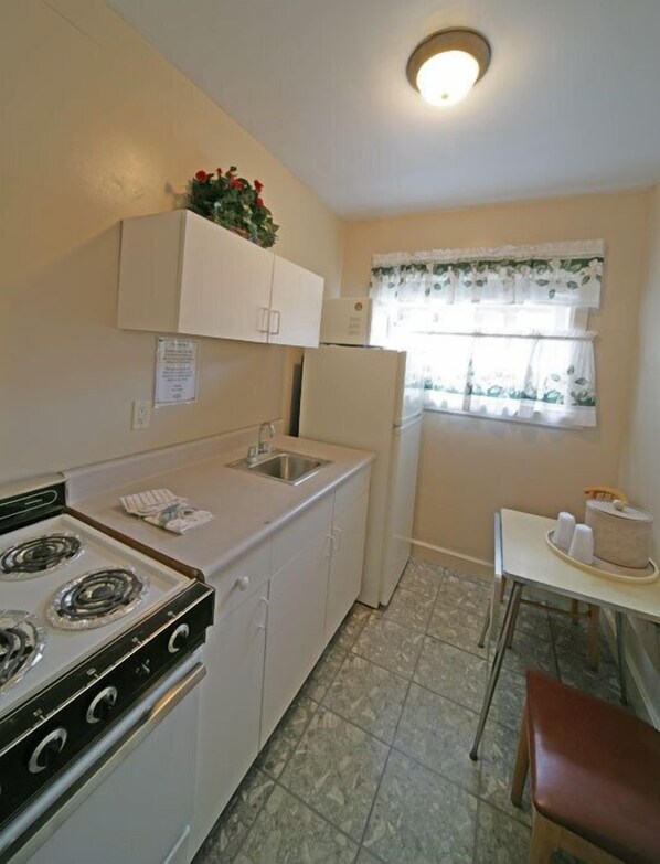 A compact kitchen with a stove, sink, and refrigerator. - Rainbow Lodge and Inn (Colorado Springs)