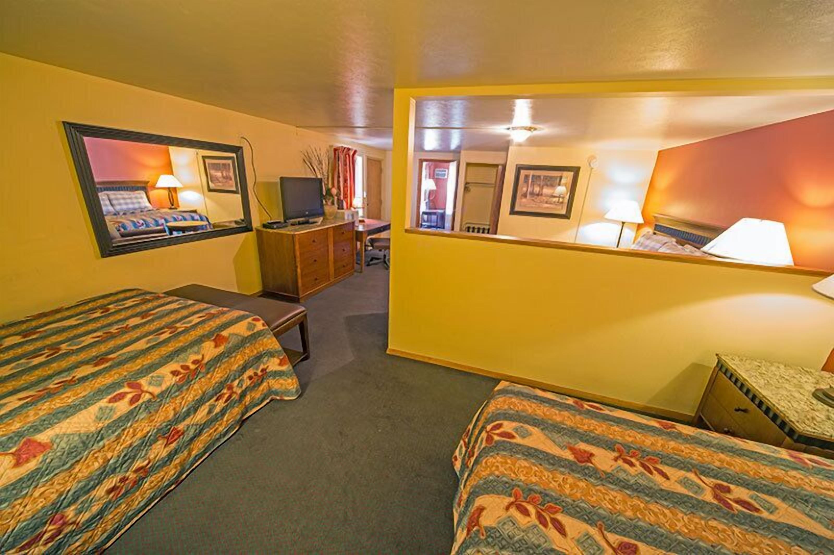 A hotel room with two beds, a desk, a television, and a mirror.