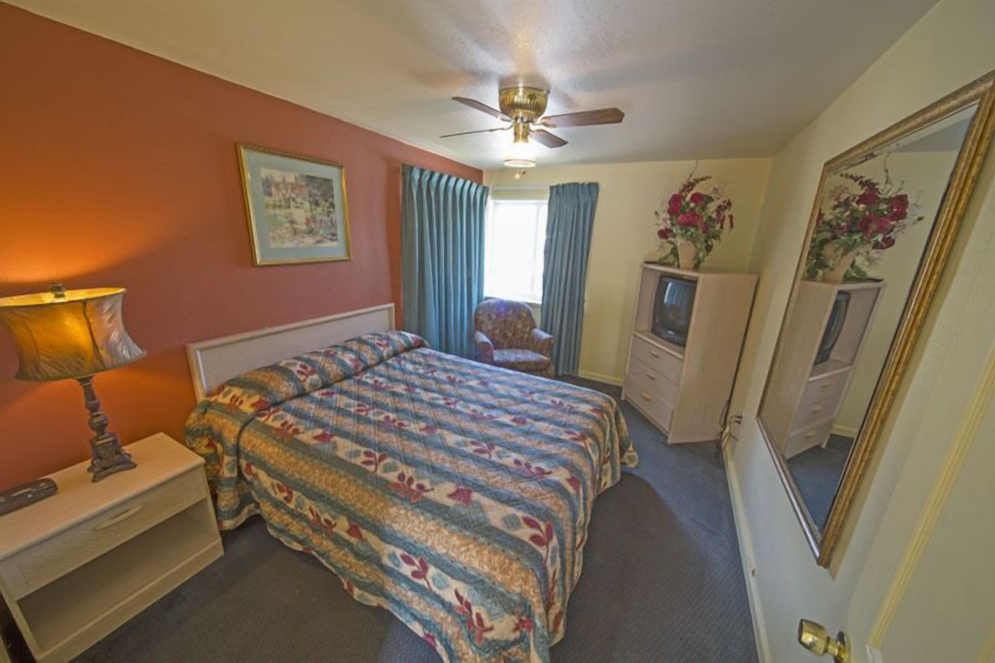 A bedroom with a bed, a nightstand, a dresser, a chair, a ceiling fan, and a mirror.
