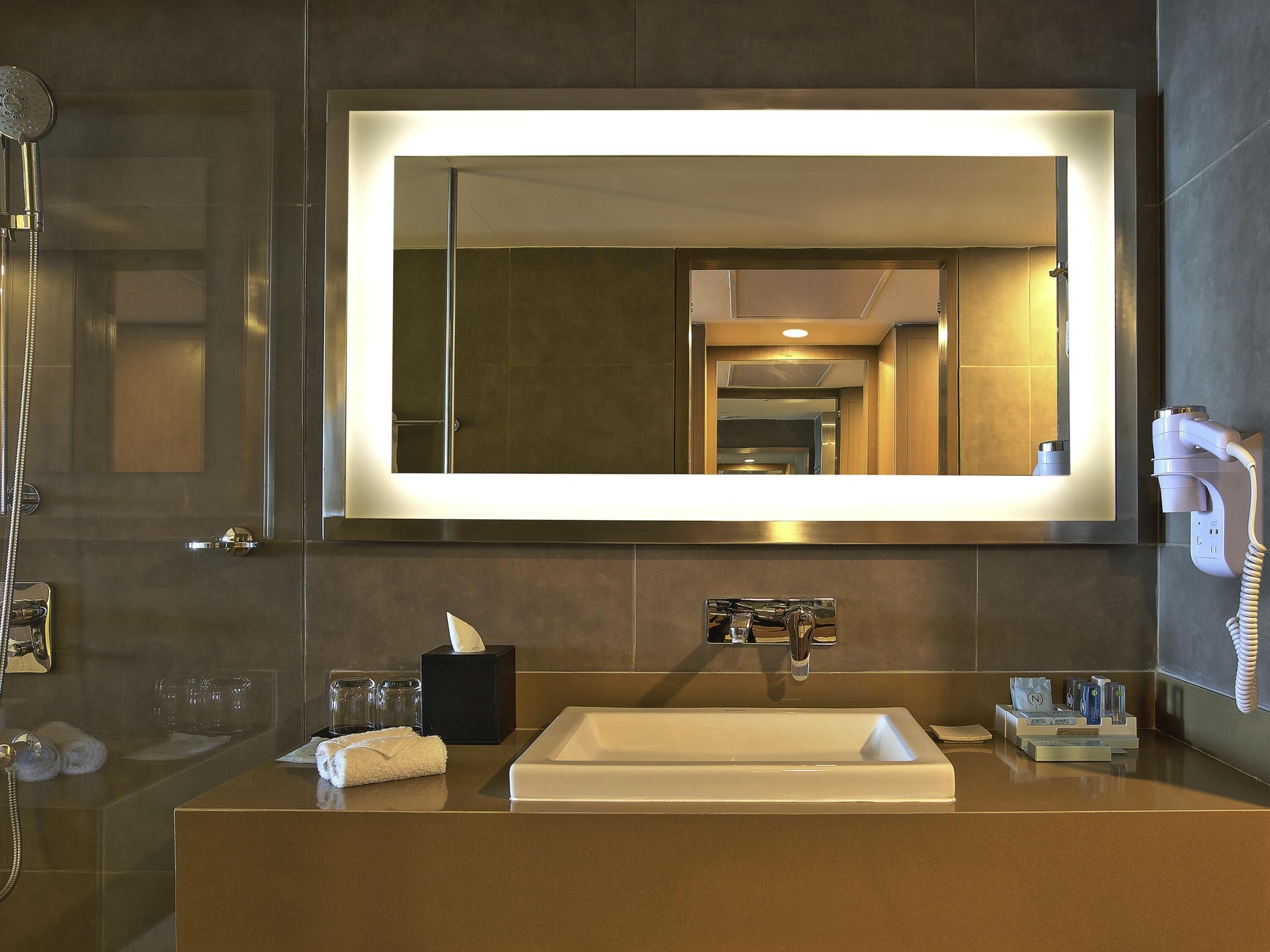A modern bathroom with a large mirror, a sink, a towel, a tissue box, and a hairdryer.