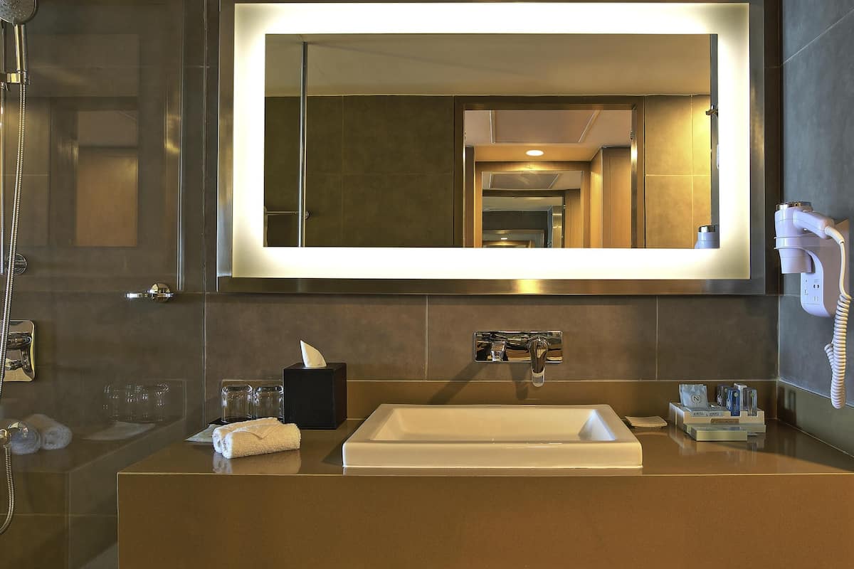 A modern bathroom with a large mirror, a sink, a towel, a tissue box, and a hairdryer.
