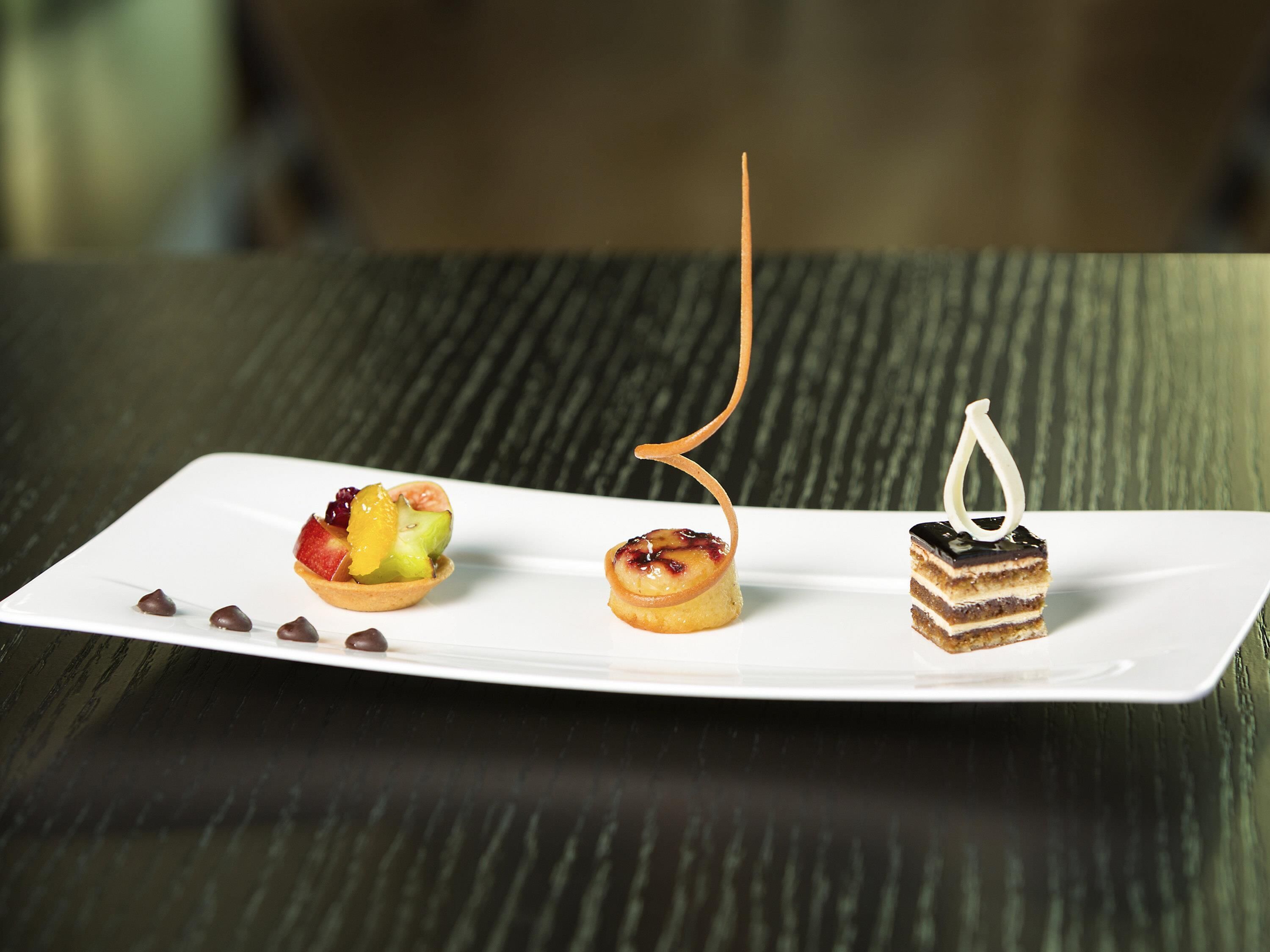 A white rectangular plate with three desserts on a textured dark surface.