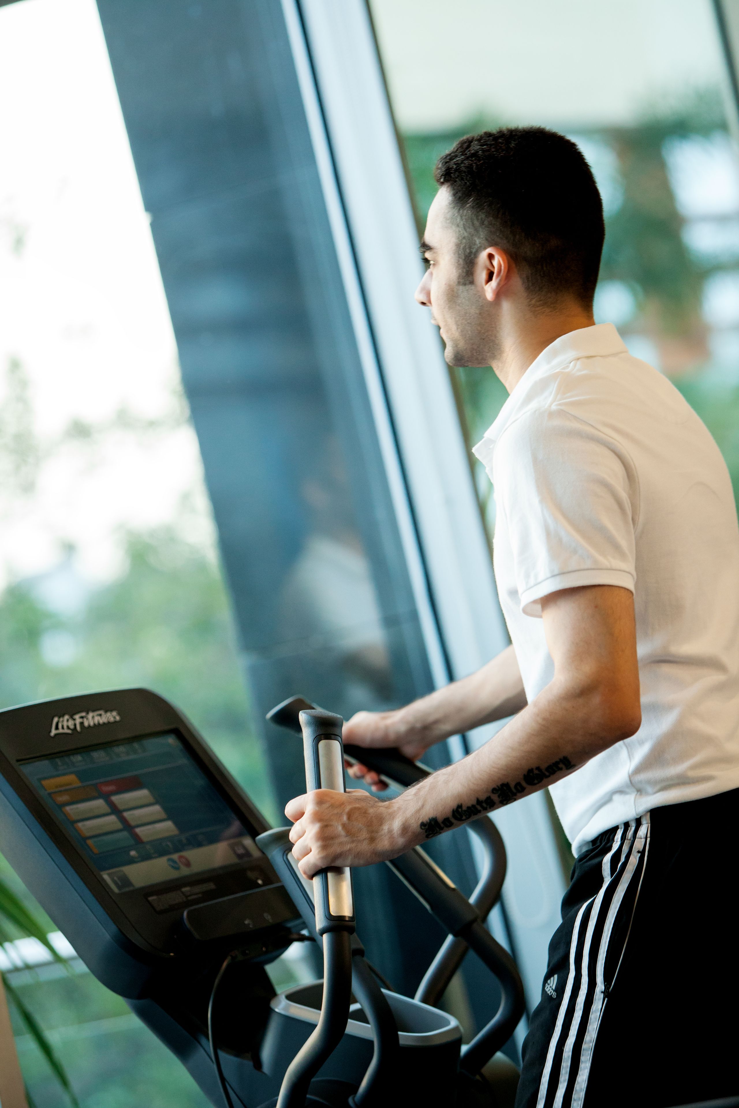 A person using a stationary bike in a gym with a large window and a control panel.
