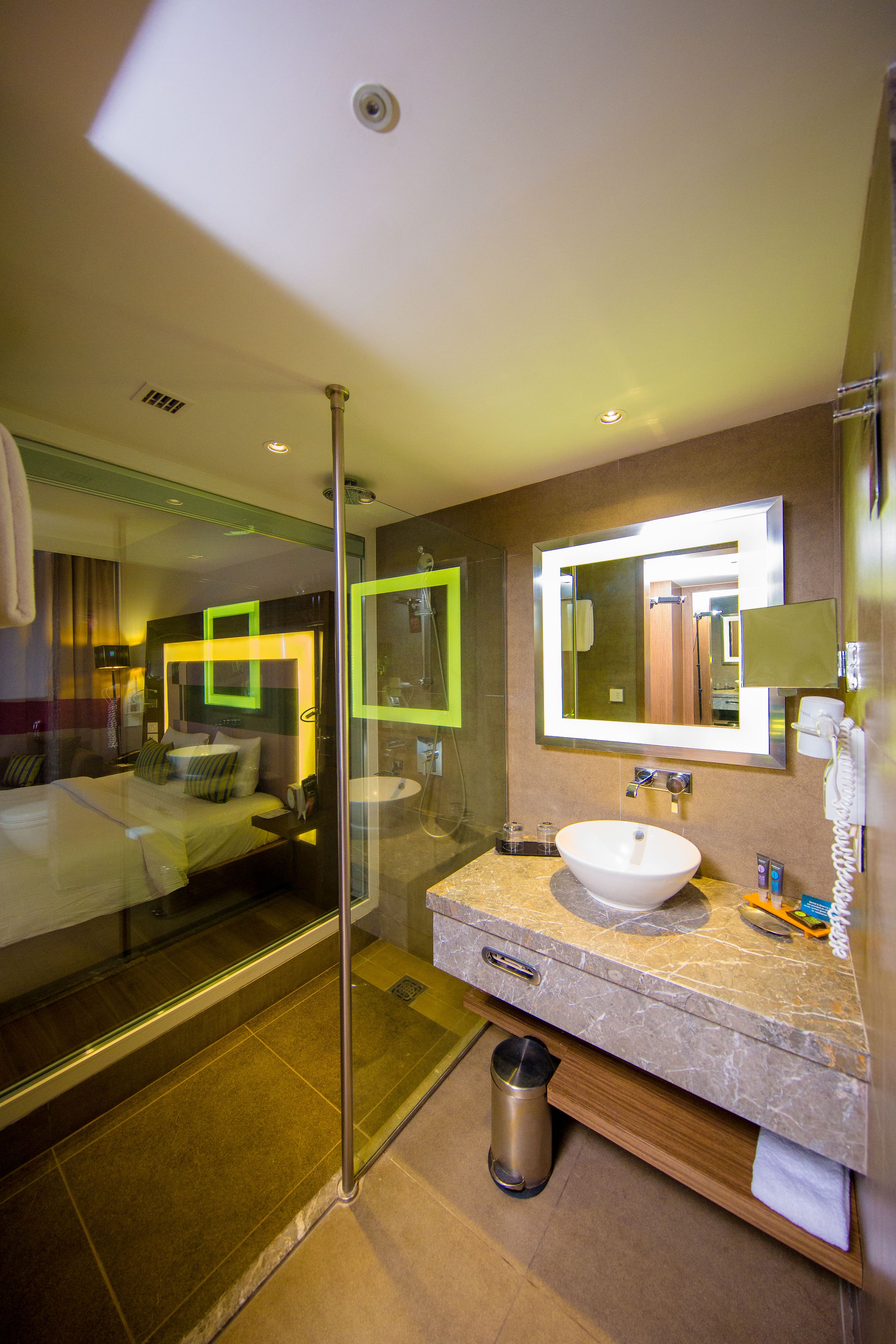 Une salle de bain d’hôtel avec une douche à parois de verre, un lavabo doté d’un plan de travail en marbre et un grand miroir au-dessus du lavabo.