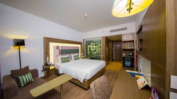 A hotel room with a bed, a desk, a chair, a sofa, a lamp, and a TV.