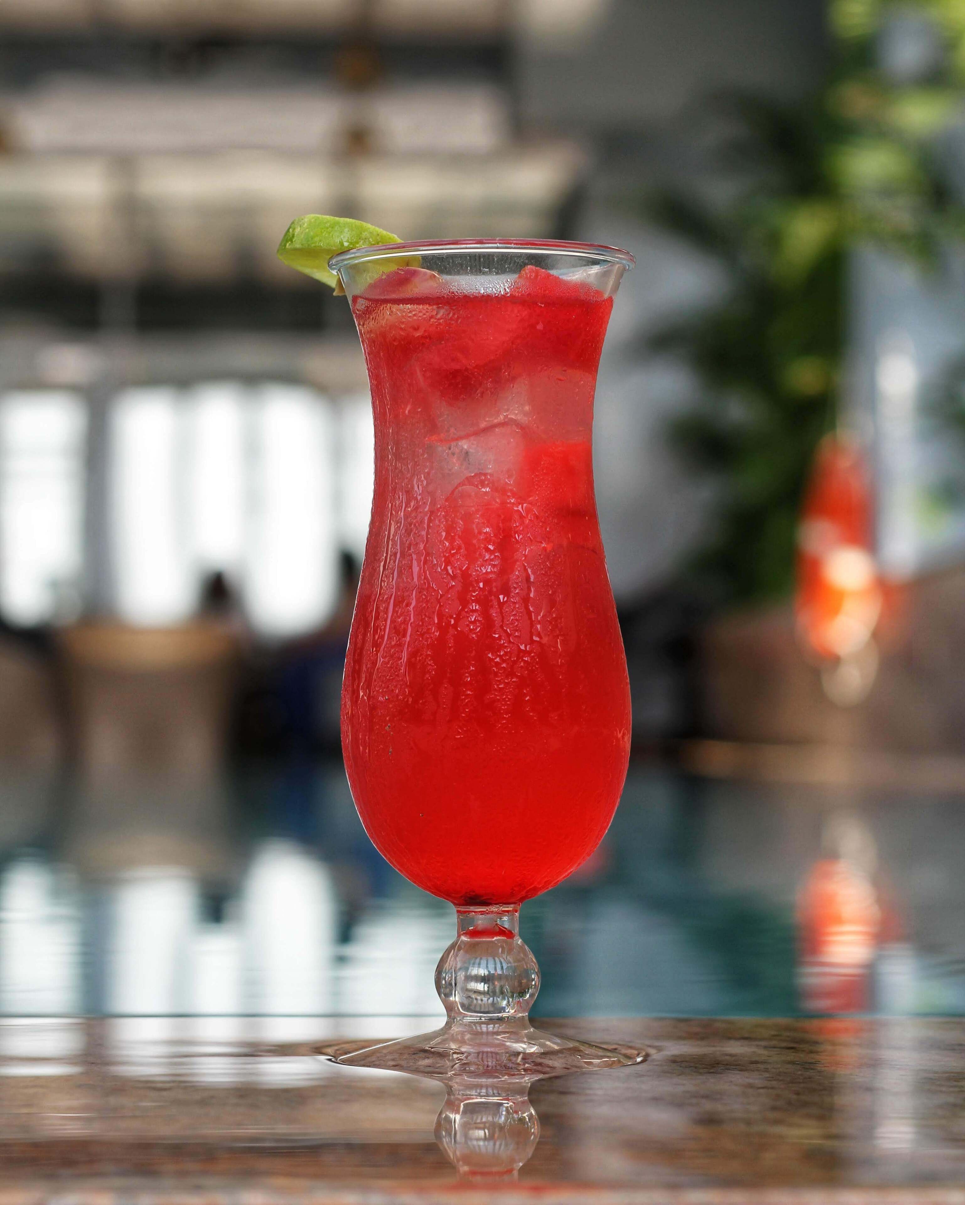 A cocktail in a tall glass with a lime garnish, placed on a reflective surface.