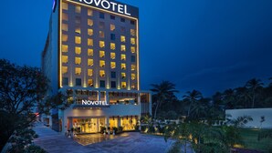 A hotel with a prominent 'NOVOTEL' sign, a ground-level entrance, and a surrounding landscaped area with palm trees. - Novotel Chennai Sipcot (Tirupporur)