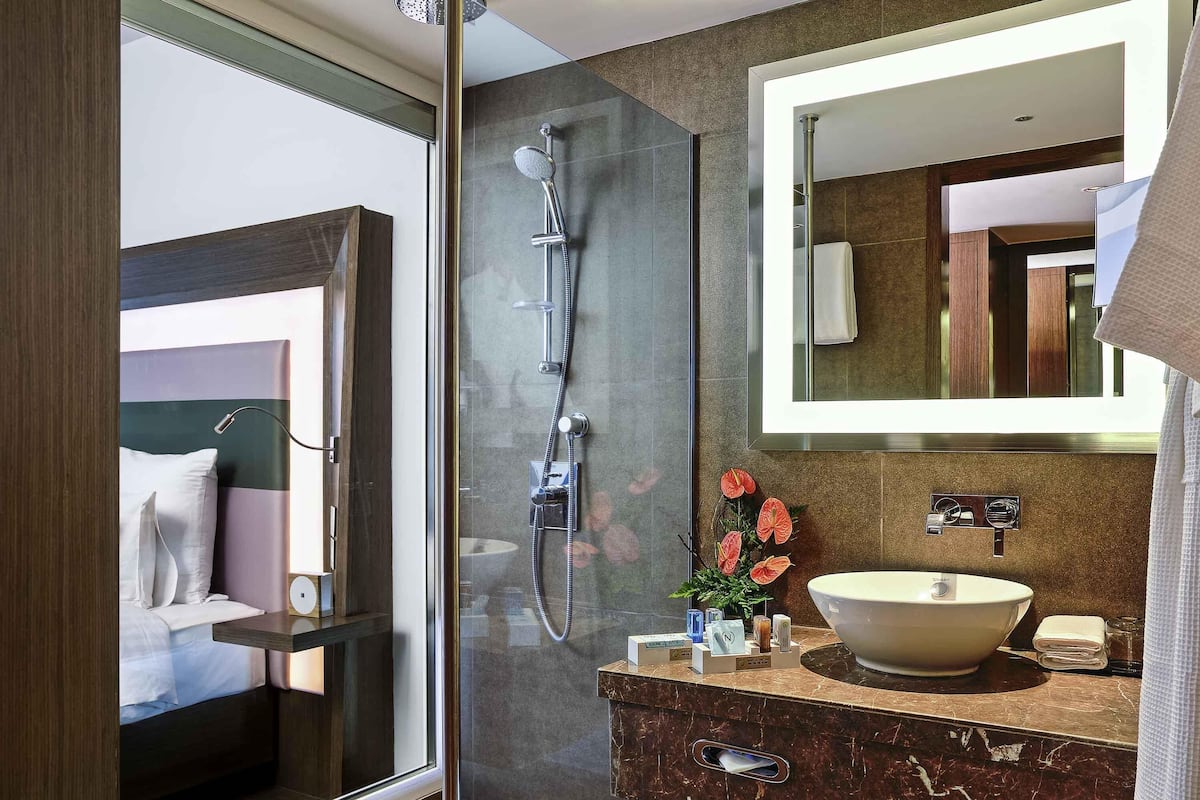 A modern bathroom with a glass shower enclosure, a marble vanity, a large mirror, and a decorative plant.