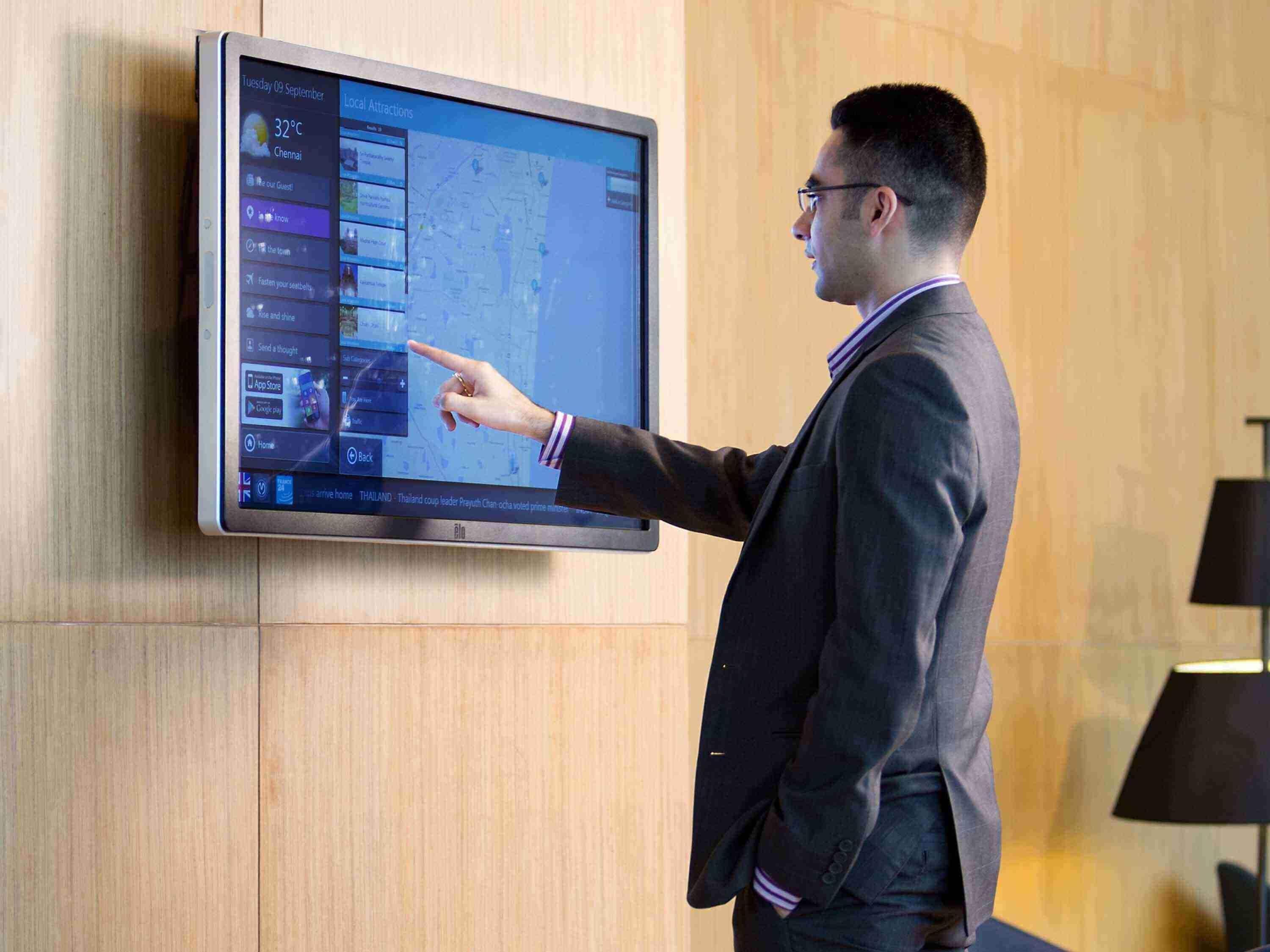 Un hombre con traje señala una pantalla digital que muestra un mapa y varios iconos de aplicaciones.