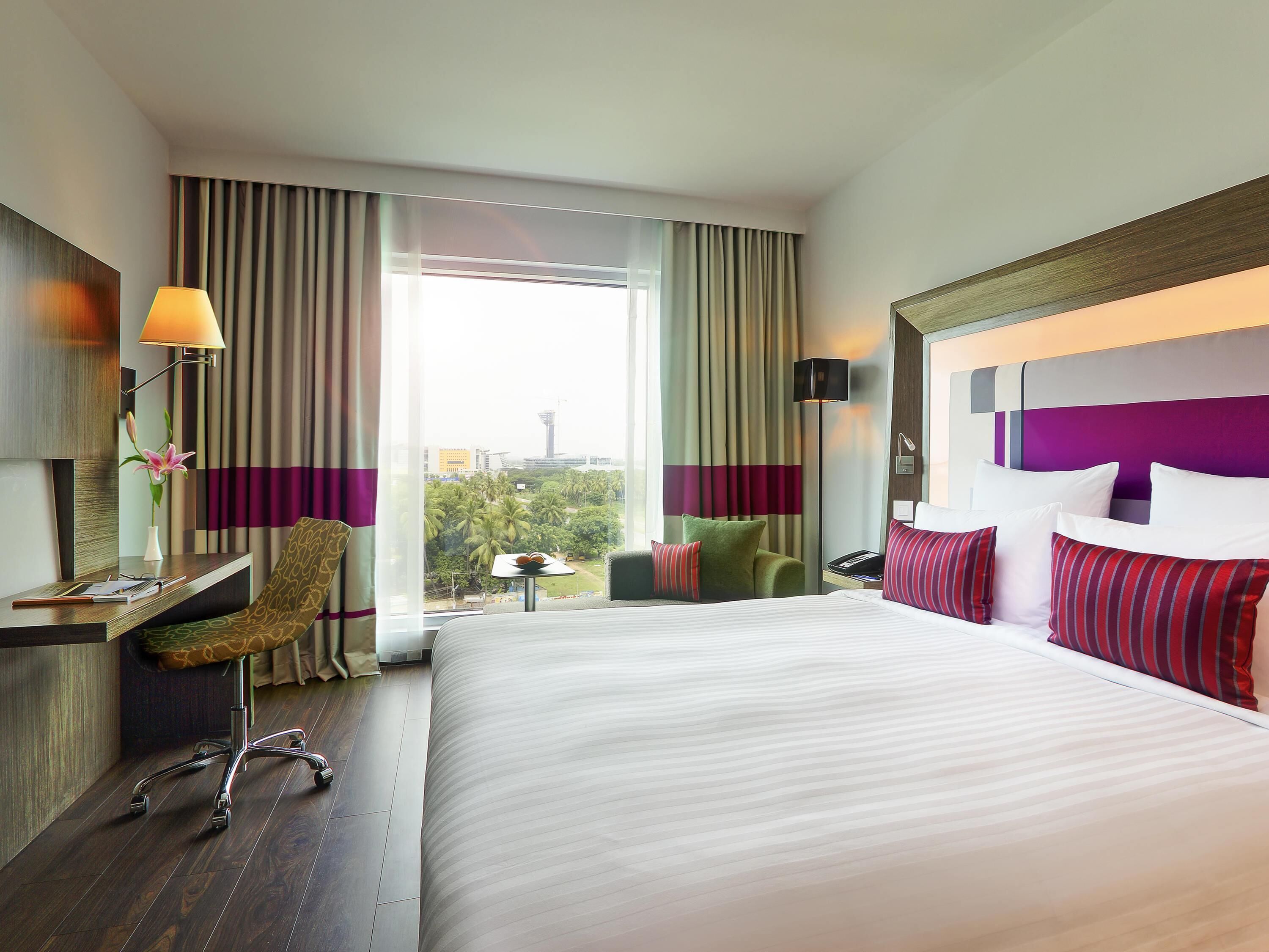 Une chambre d’hôtel avec un grand lit, un bureau avec une lampe, une chaise et une vue sur le paysage urbain.