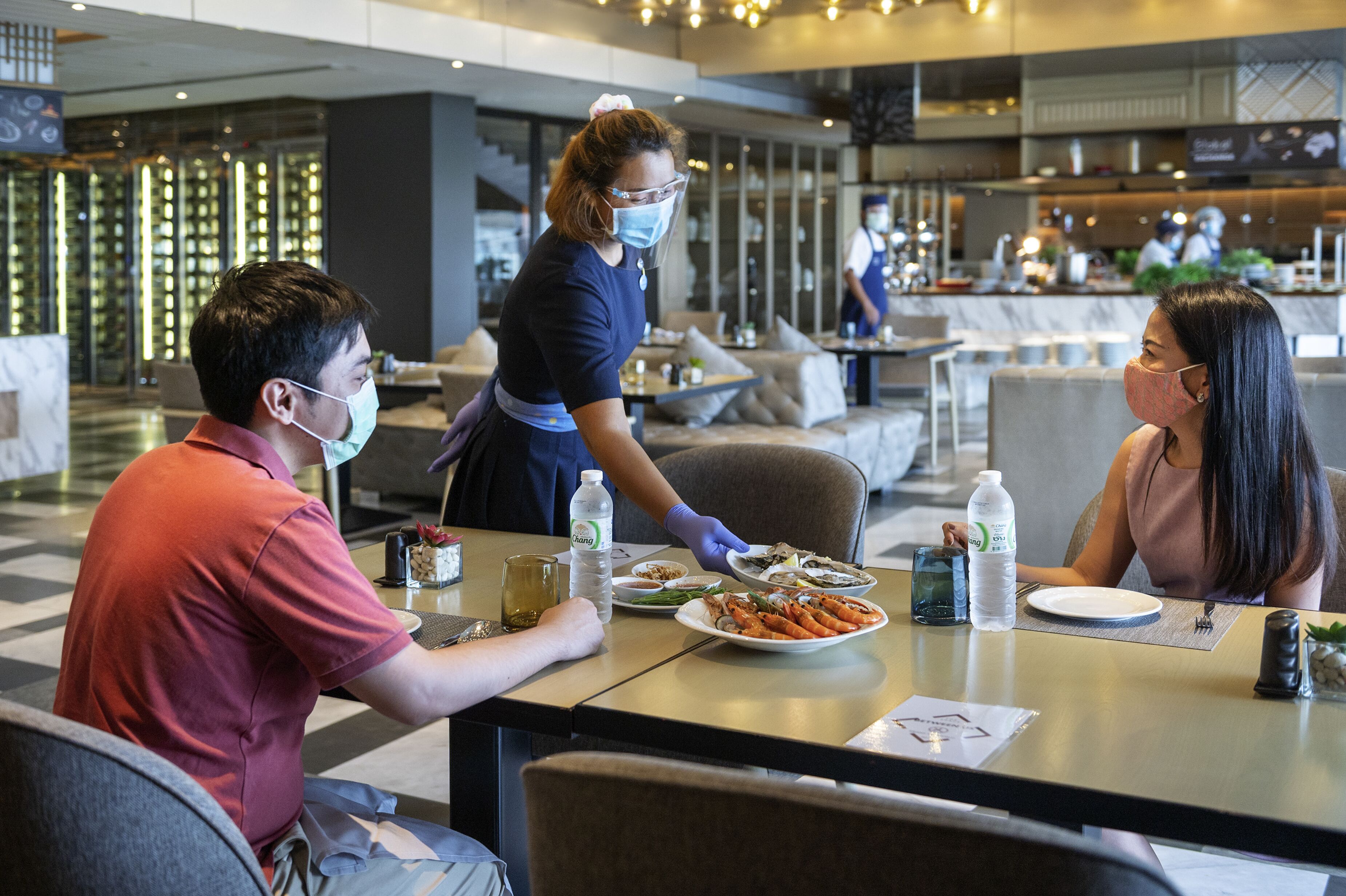 Une scène de restaurant où un serveur apporte des plats aux clients assis à une table.