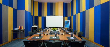 A conference room with a long table, chairs, a projector screen, and a presentation screen.