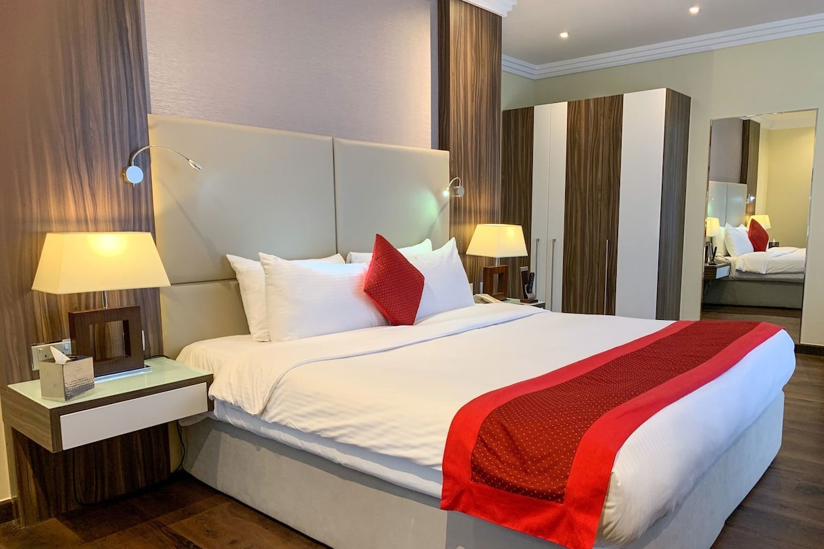 Ein Hotelzimmer mit einem großen Bett, zwei Nachttischen mit Lampen, einem Spiegel und einem Kleiderschrank.