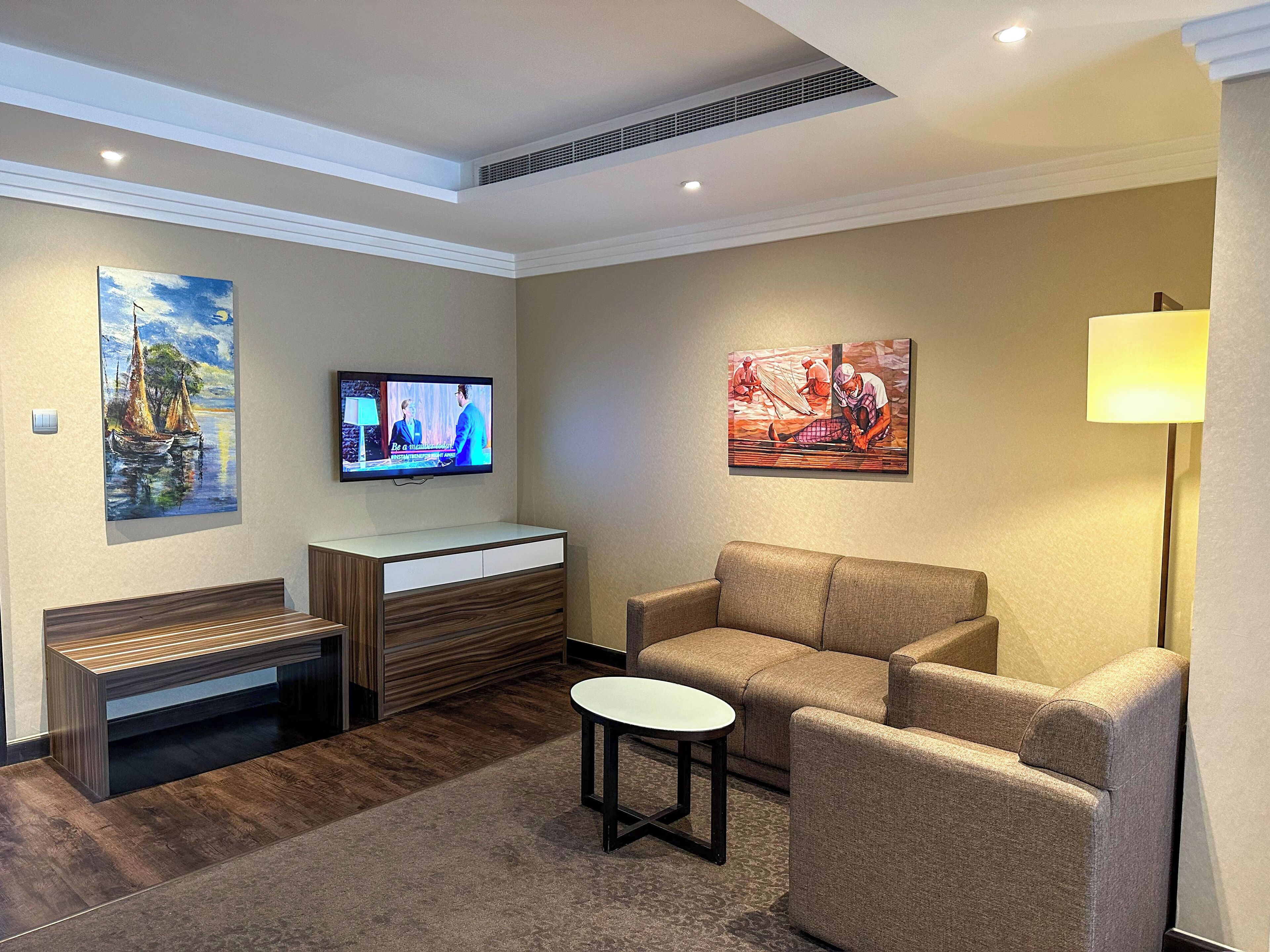 Una habitación de hotel moderna con una televisión de pantalla plana, un sofá, una mesita y obras de arte en las paredes.
