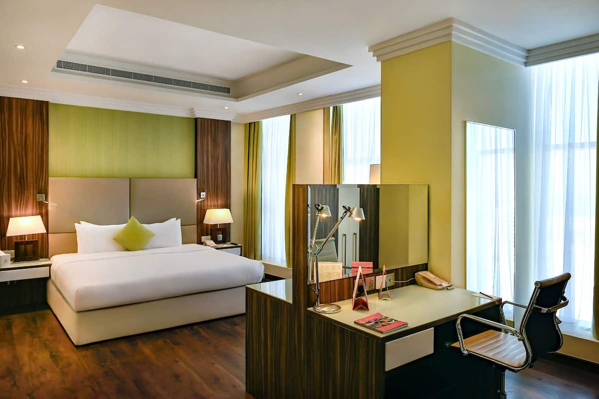 A hotel room with a bed, desk, chair, and large windows.
