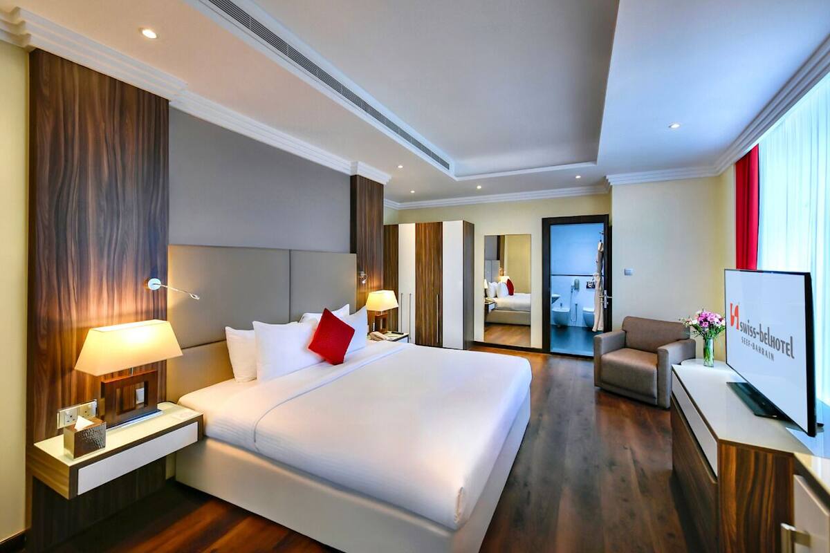 A modern hotel room with a large bed, bedside lamps, a TV, and a desk with a computer.