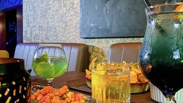 A bar area with a variety of drinks, including a green cocktail, a yellow drink, and a dark green drink with a straw. There are also snacks and a decorative candle on the table.