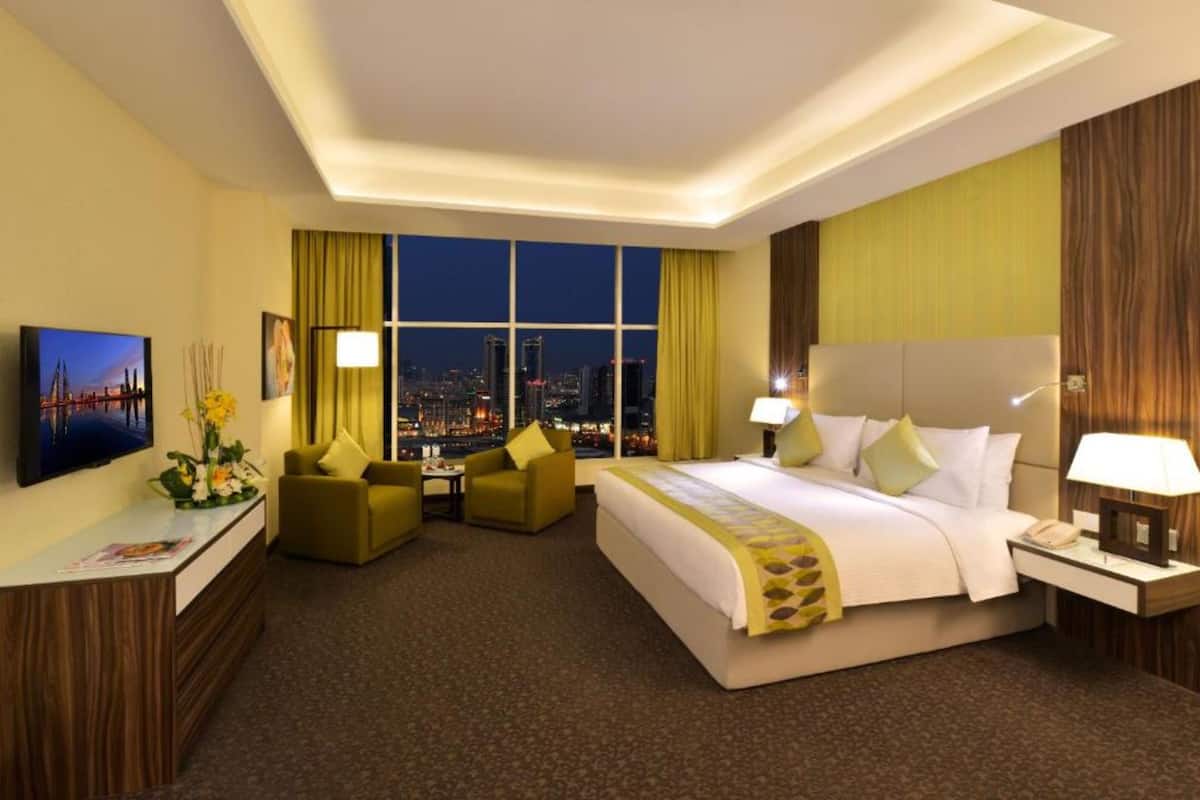 A hotel room with a large bed, a desk with a computer, a chair, and a view of a cityscape at night.