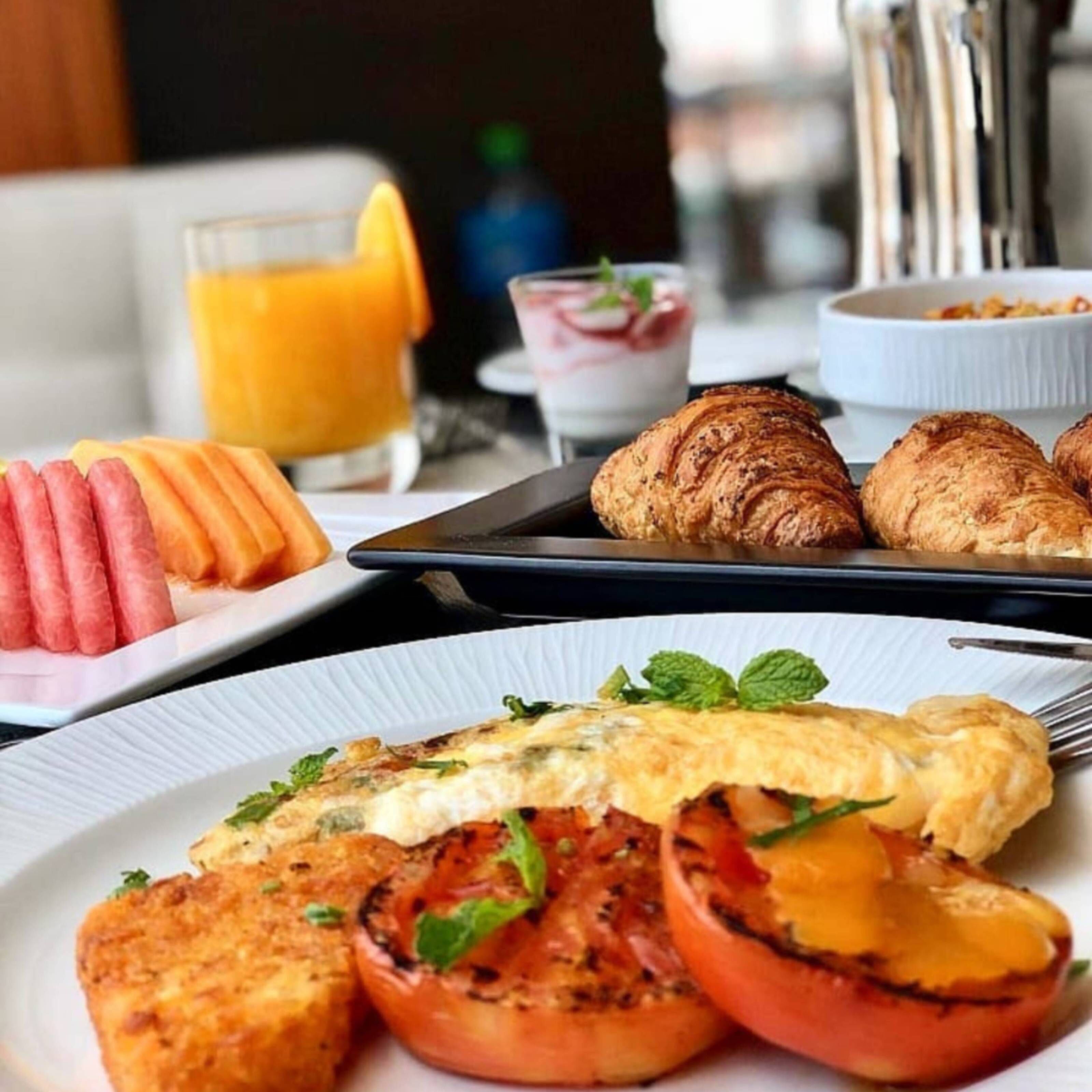 A breakfast setting with croissants, grilled tomatoes, and a plate of scrambled eggs.