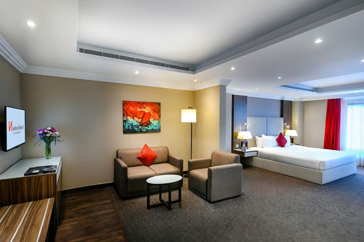 A hotel room with a bed, two sofas, a small table, a desk, and a painting on the wall.