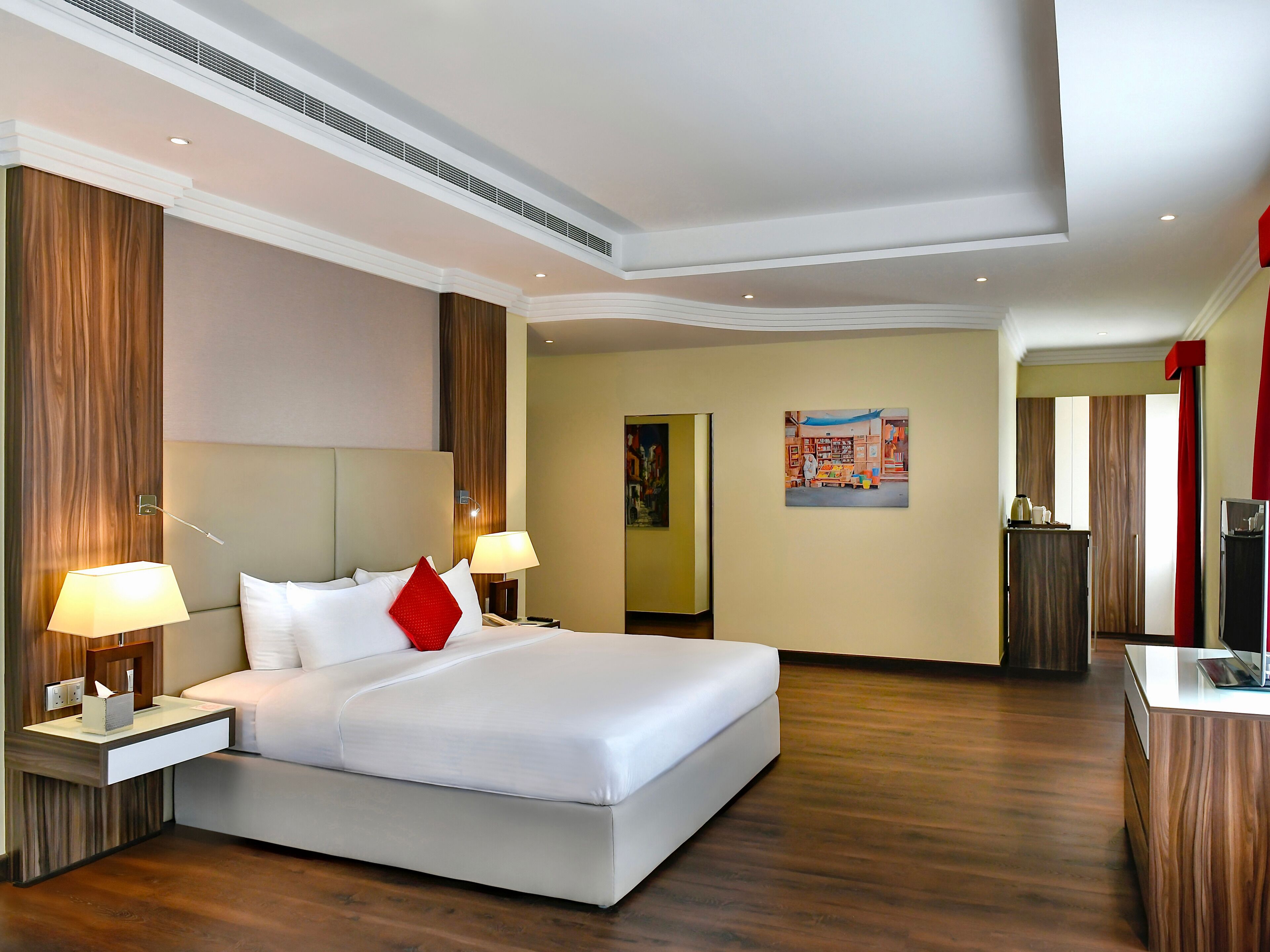 Une chambre d’hôtel moderne avec un grand lit, deux tables de chevet avec des lampes, un mur décoratif en bois, un tableau et un bureau avec un ordinateur.