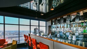 Un bar con vistas a la ciudad, taburetes rojos y una gran variedad de botellas y vasos.