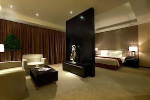 A hotel room with a bed, a sofa, a coffee table, a decorative sculpture, and a nightstand with a lamp.