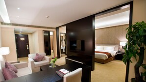 A hotel room with a bed, a desk, a chair, a TV, and a potted plant.