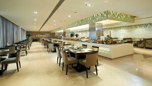 A modern dining area with multiple tables and chairs, a buffet with various food items, and a decorative ceiling.