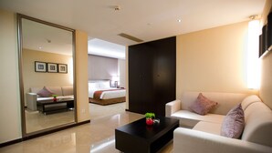 A modern hotel room with a large mirror, a sofa, a coffee table with a plant, and a bed with a red blanket.