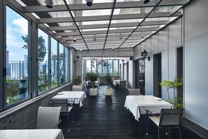An indoor dining area with tables and chairs, large windows, and potted plants. - JB Design Hotel Haeundae (Busan)