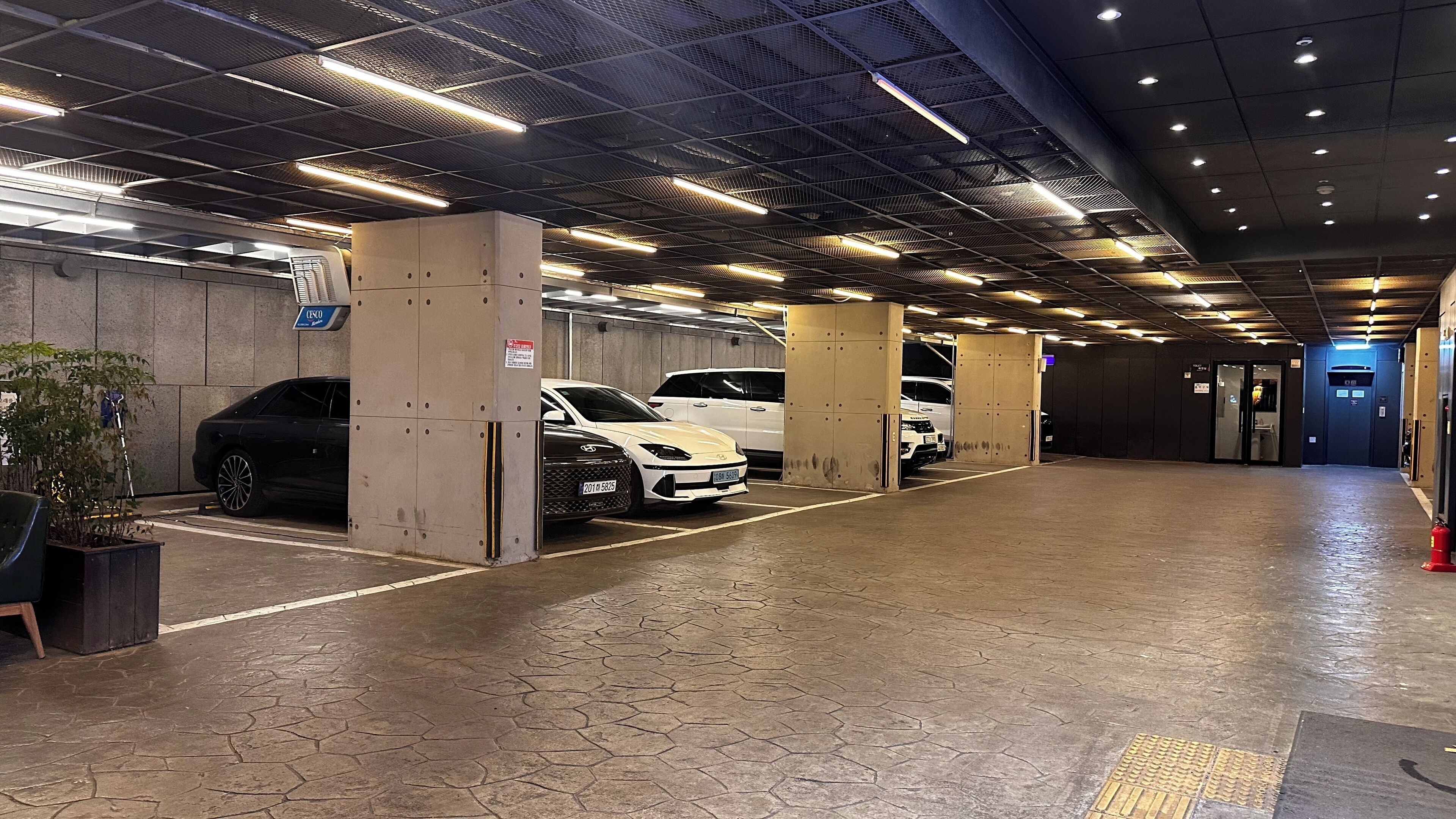 A multi-level parking garage with concrete pillars, hexagonal patterned flooring, and overhead lighting.