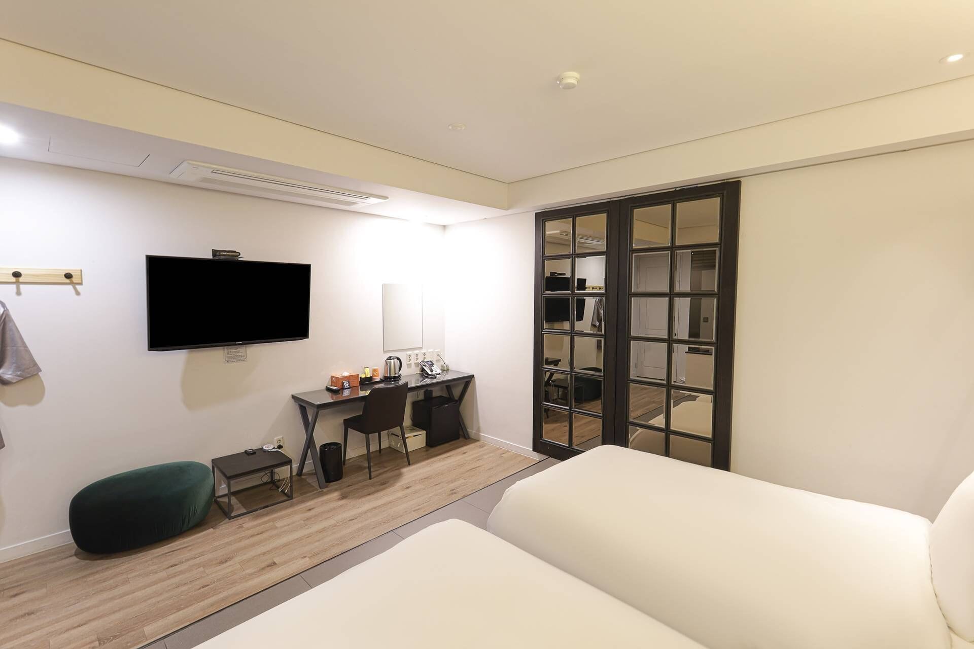 Ein Hotelzimmer mit Bett, Schreibtisch mit Stuhl, Fernseher, Spiegel und Kleiderschrank mit Schiebetür.